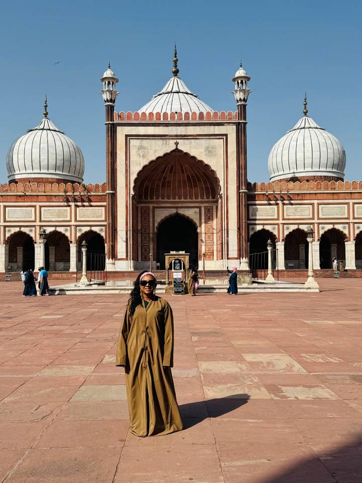 Visitor stands in the courtyard of Jama Masjid with majestic domes and arched entrance behind.