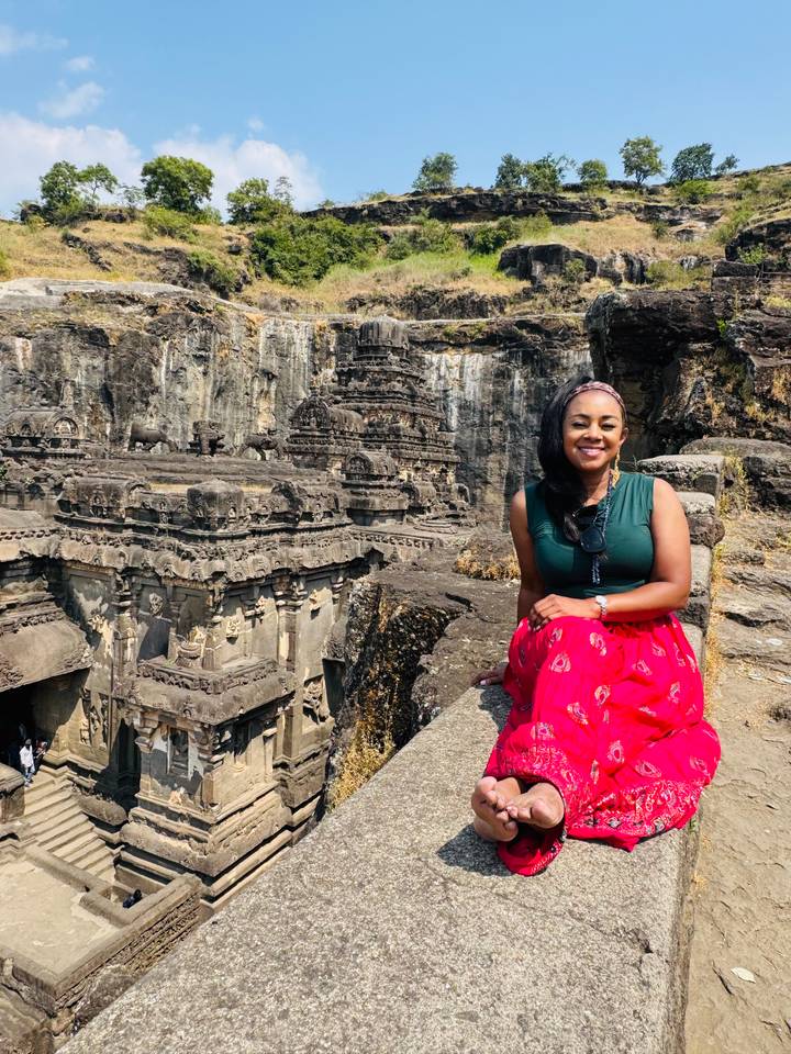 Traveler sitting beside elaborate rock-cut temple structures carved into a cliff face.