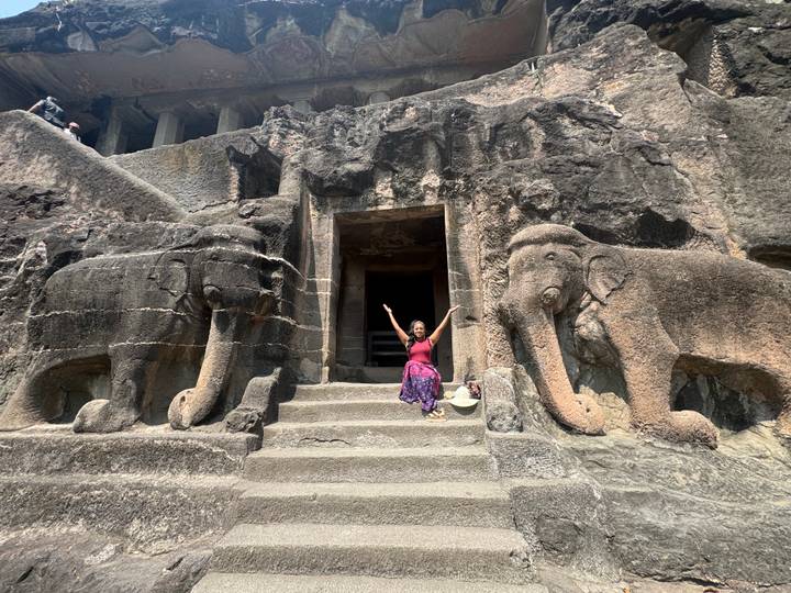 Visitor poses triumphantly between two huge elephant carvings flanking a cave temple entrance.
