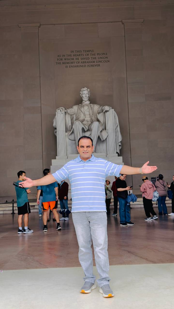 Smiling man with open arms poses in front of the seated Lincoln statue inside the Lincoln Memorial