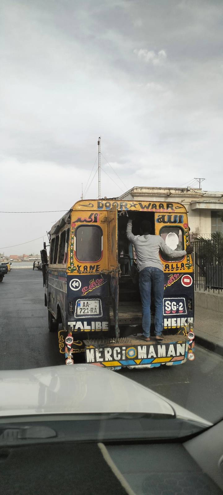 Colorful vintage bus with hand-painted decorations loading passengers on a riverside street