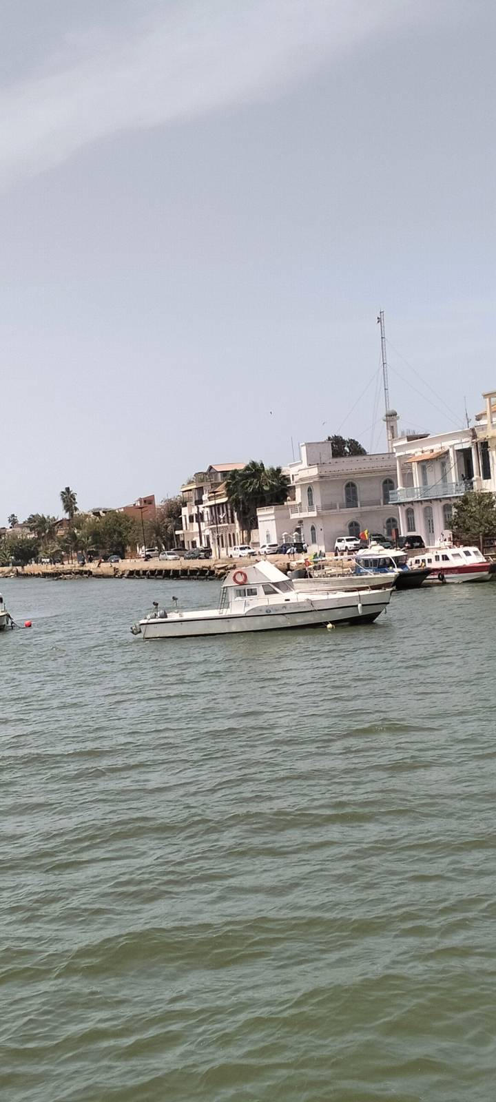 Small leisure boats float on a calm river lined with colonial buildings and palms
