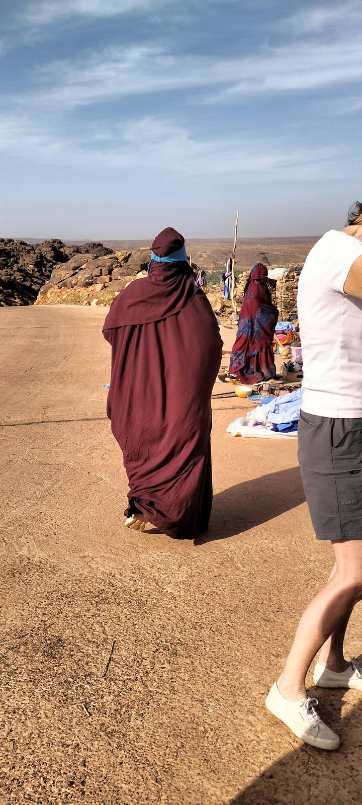 Partial view of a robed person standing beside scattered market goods, poorly framed