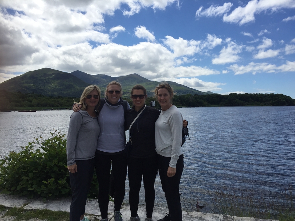 Quatre femmes posant au bord d'un lac avec des montagnes en arrière-plan.