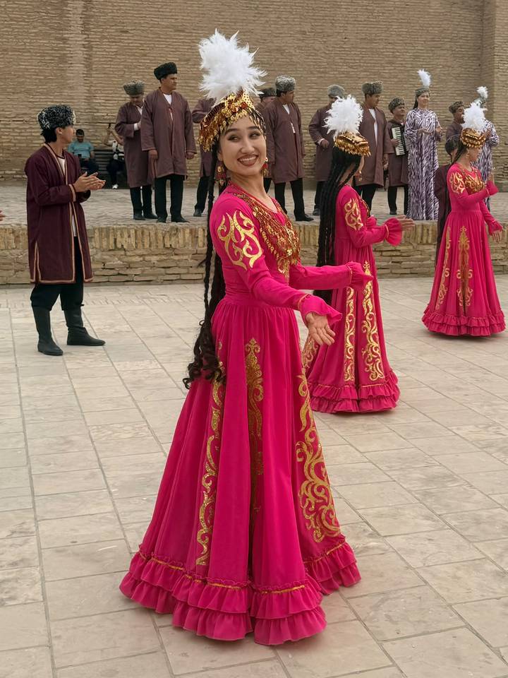 Women in bright pink traditional dresses performing a folk dance in a historic brick courtyard