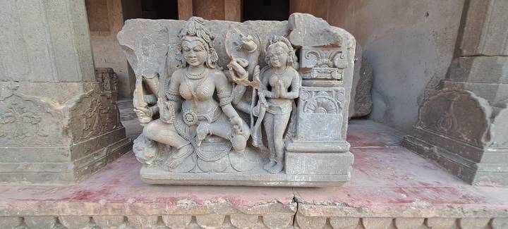 Stone sculpture of Hindu deities displayed on a plinth within an ancient complex