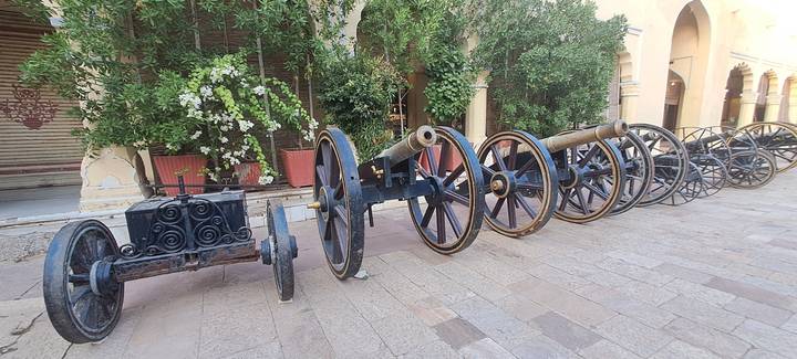 Row of antique cannons lined up in a palace courtyard with green foliage behind