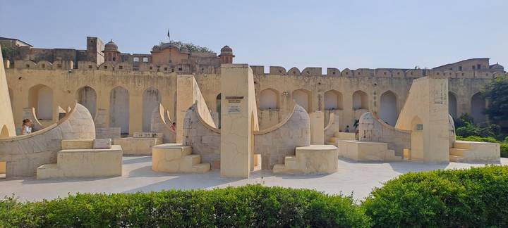 Sunlit stone instruments of Jantar Mantar observatory set against fortress walls