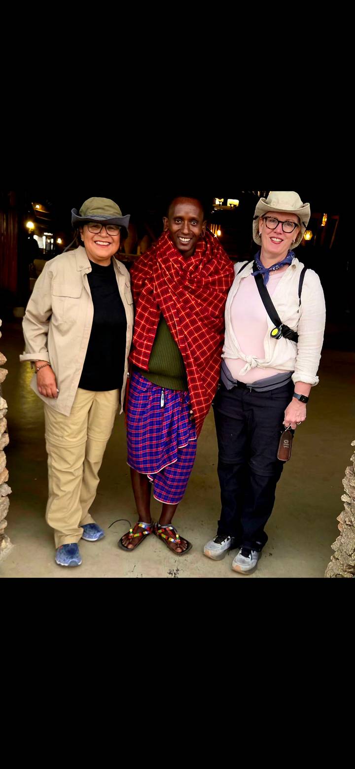 Three people standing with a traditionally dressed Maasai host inside a building.