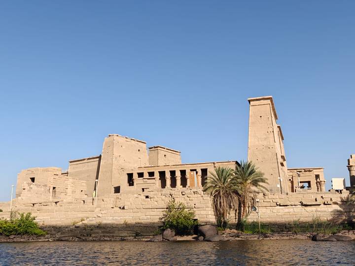 Island temple complex of Philae framed by a clear blue morning sky and a lone palm.