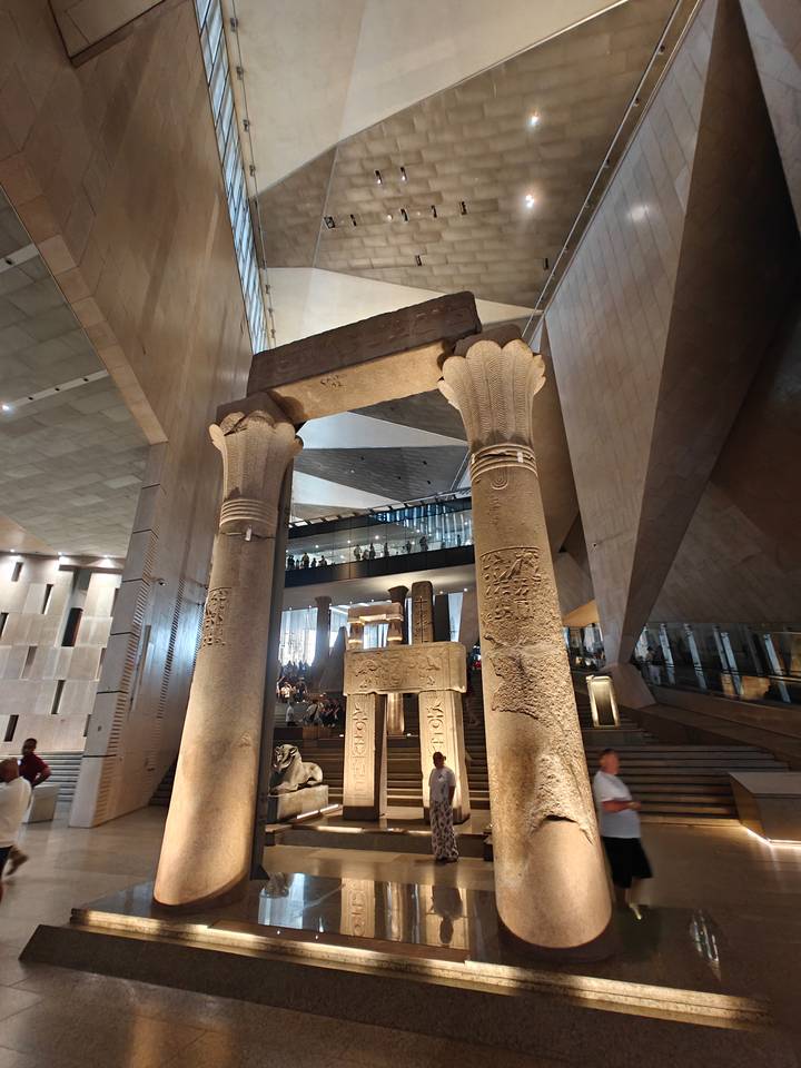 Massive ancient columns inside a modern museum atrium with visitors viewing exhibits on multiple levels.