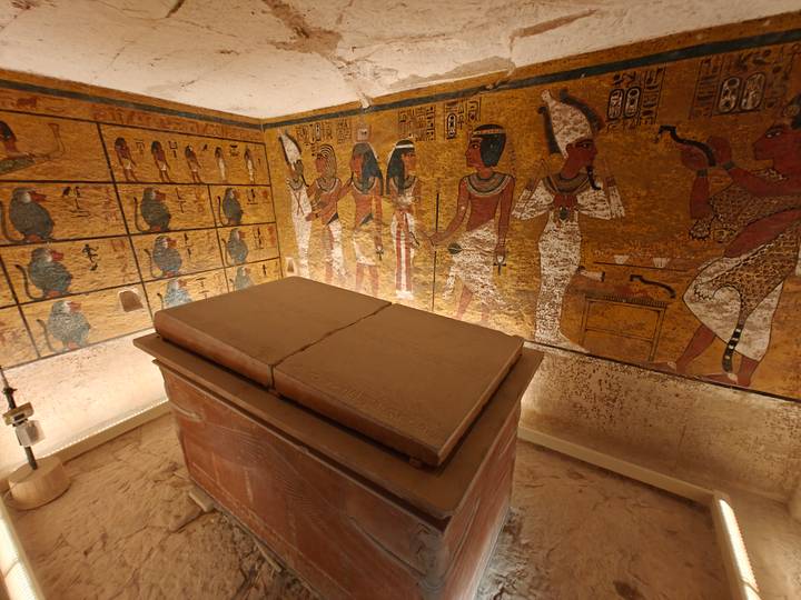 Interior of an Egyptian tomb decorated with colorful hieroglyphic murals and a stone sarcophagus.
