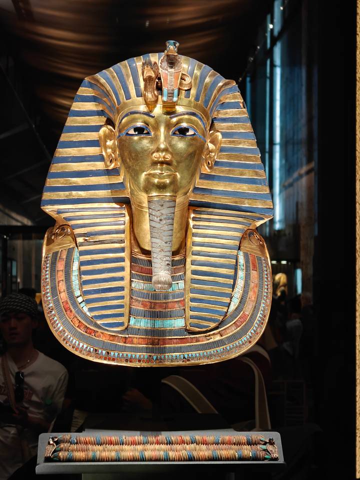 The golden funerary mask of Tutankhamun glistens under museum lights.