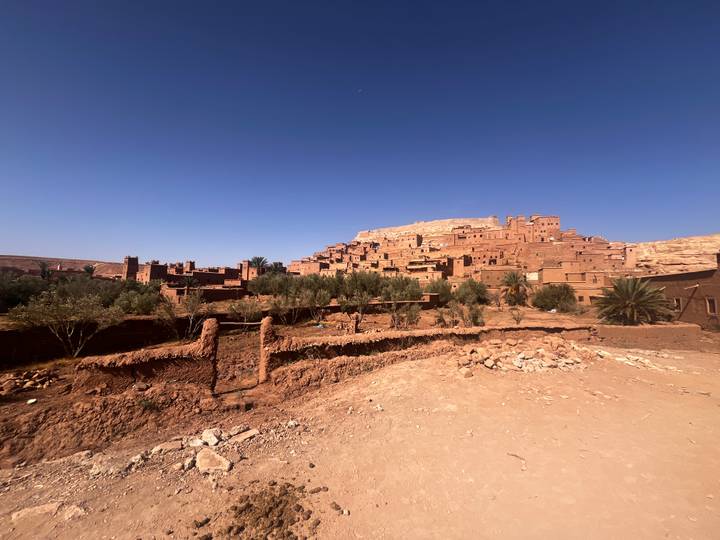 Adobe ksar of Ait Benhaddou rises above palm groves under cloudless desert sky
