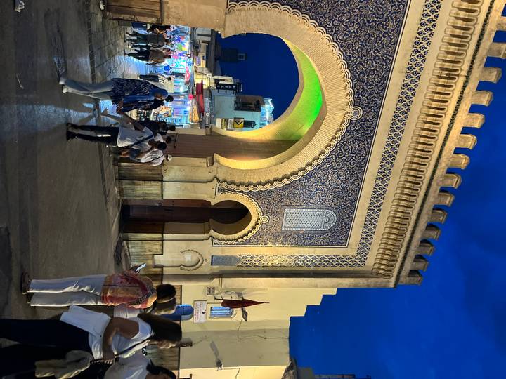 Night scene at the ornate Blue Gate with tourists milling under colorful lights