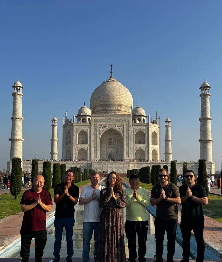 Six travellers posing in front of the iconic Taj Mahal on a clear day