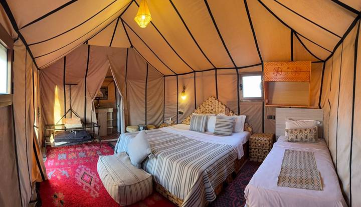 Spacious canvas desert camp tent with king bed, patterned rugs and warm ambient lighting.