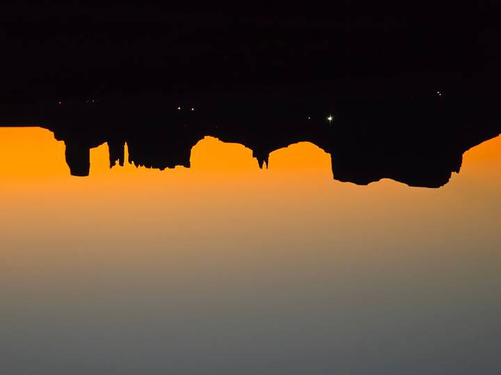 Silhouetted mesas of Monument Valley stand against a vivid orange sunrise horizon.