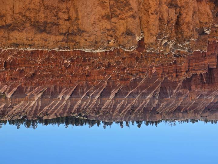 Steep red hoodoos and striped cliffs fill the amphitheatre of Bryce Canyon under a clear sky.