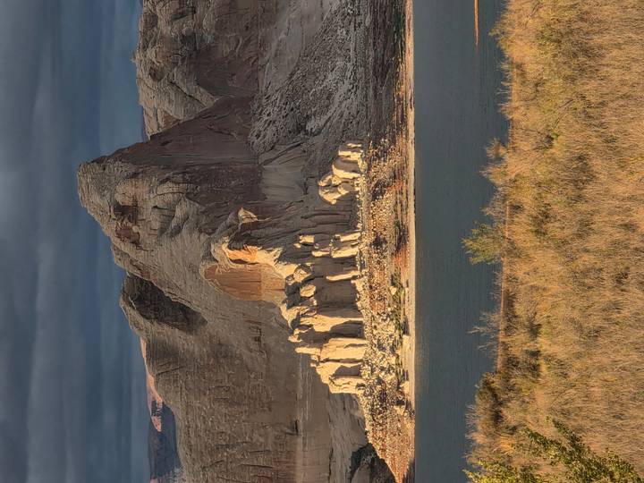 Sunlit rock formations rise from Lake Powell’s shoreline beneath brooding storm clouds.