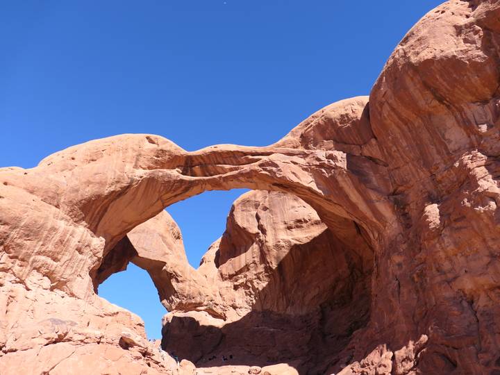Massive red sandstone arches intertwine against a cloudless blue sky in Arches National Park.