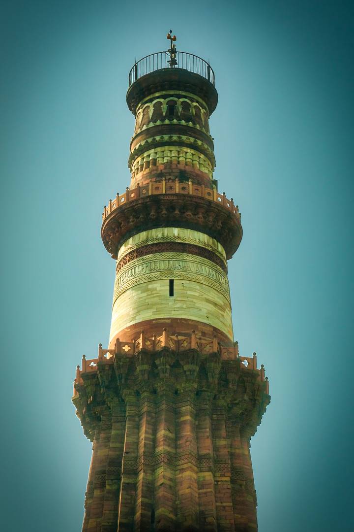 Detailed close-up of the ornate minaret of Qutub Minar with Arabic calligraphy against a clear sky.