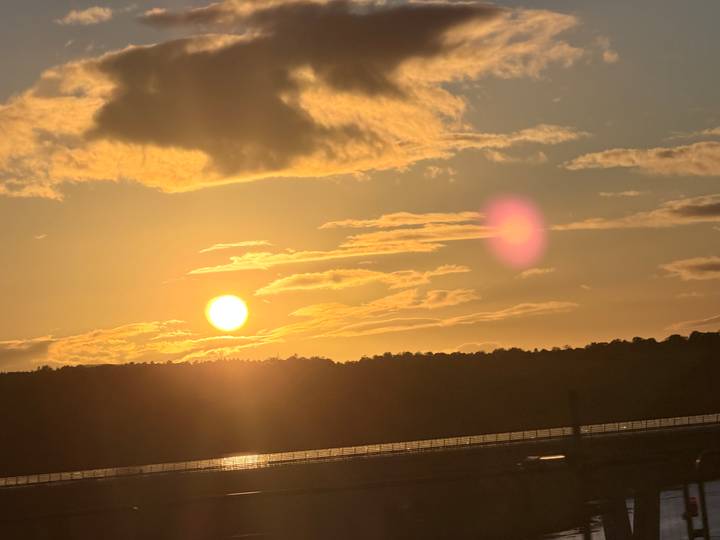 Golden sunset over a forested horizon with bright sun and pink lens flare in the sky.