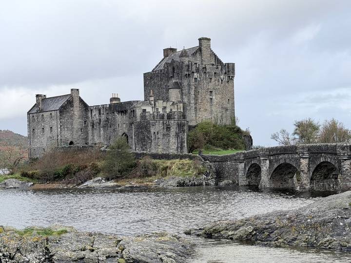 Historic Eilean Donan Castle and stone bridge set against misty hills beside a loch.
