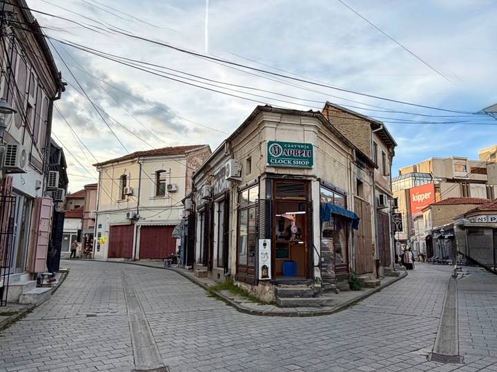 Narrow cobblestone street lined with historic shopfronts and overhead cables in Bitola’s old bazaar.