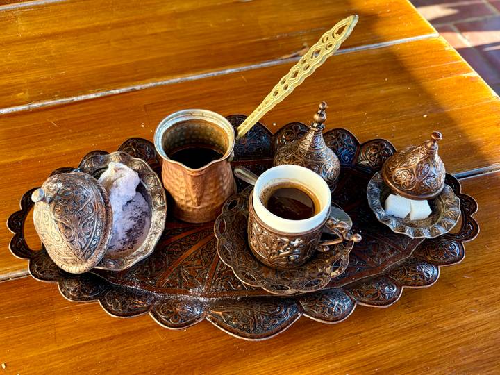Intricately carved copper coffee set with traditional cups, pot and sugar on a decorative tray.