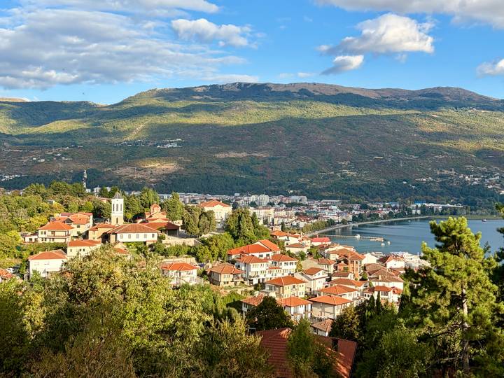 Panoramic view over Ohrid town with red-roofed houses, lakeshore promenade and surrounding mountains.
