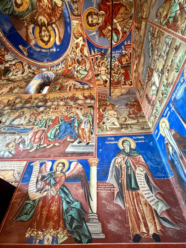 Colorful frescoes covering church walls depicting biblical scenes and saints with vivid blues and reds.