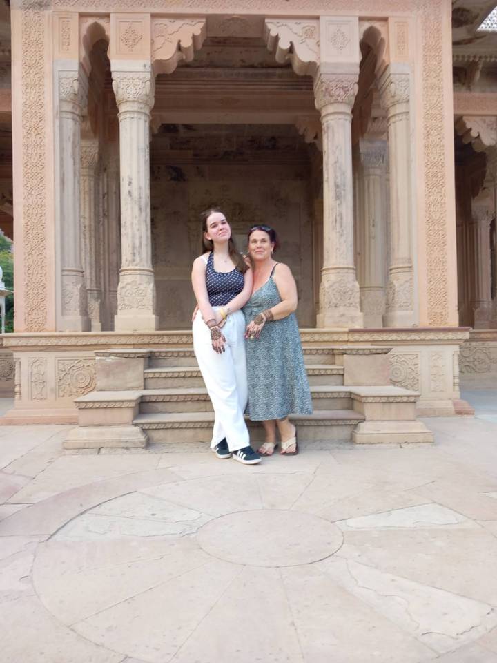 Two women posing in front of intricately carved sandstone pillars.