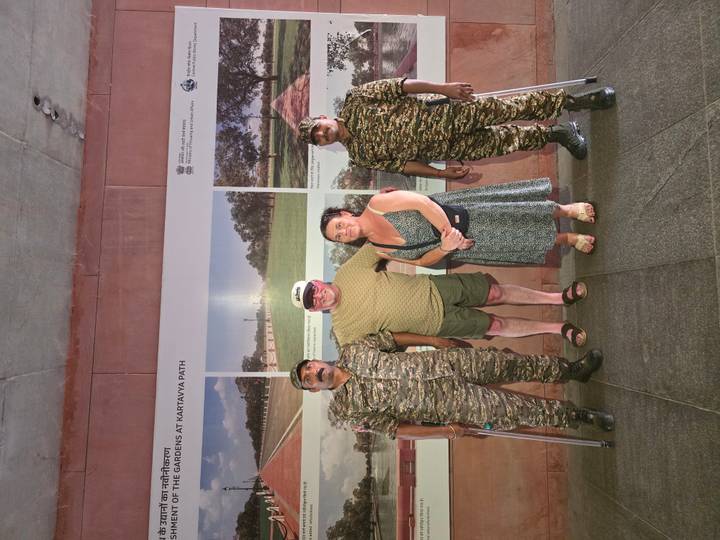Tourists posing with two uniformed guards in front of a Kartavya Path display panel.