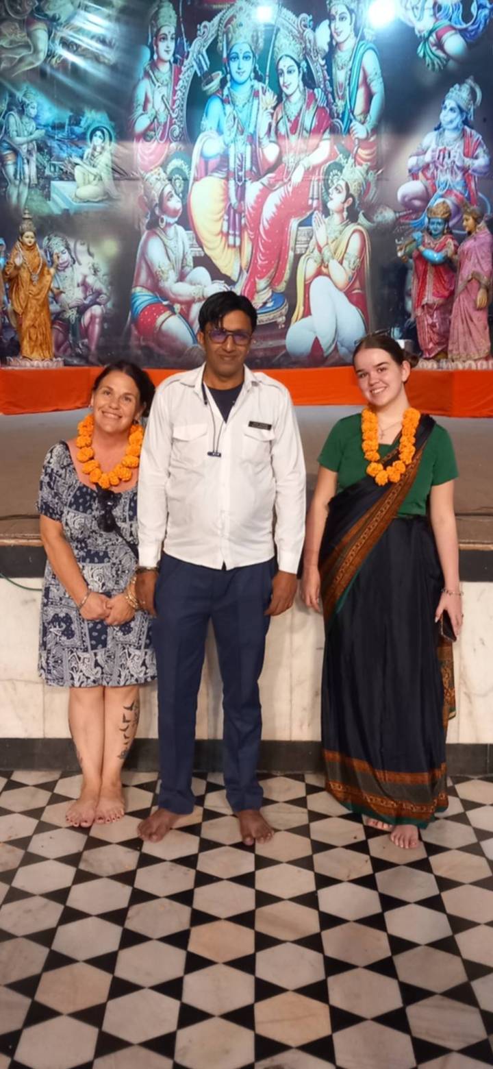 Three travellers wearing marigold garlands standing together at an indoor event.