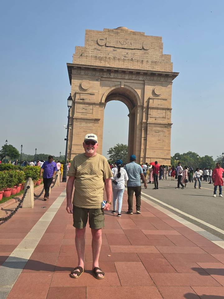 Tourist standing in front of the towering India Gate surrounded by crowds.
