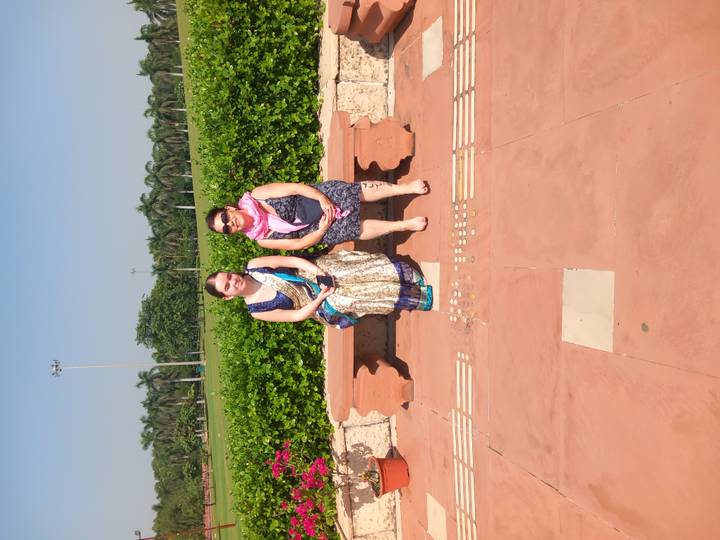 Two women in traditional dress seated on a stone bench in a manicured park.