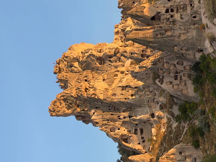 Sunlit fairy-chimney rock castle in Cappadocia glowing golden against a clear blue sky.