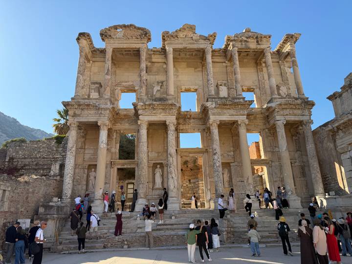 Visitors explore the grand façade of the Library of Celsus in Ephesus under clear blue skies.