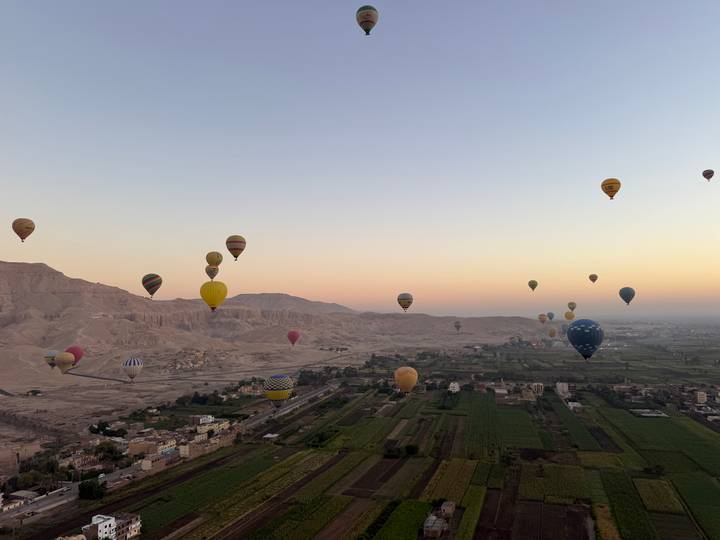 Dozens of colorful hot air balloons drift above the Nile Valley and desert cliffs at dawn near Luxor.
