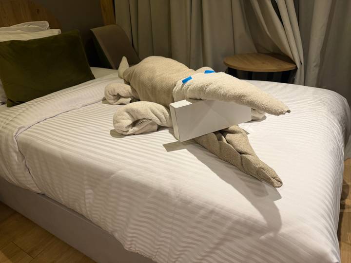 Playful towel sculpture of a crocodile on a neatly made hotel bed.