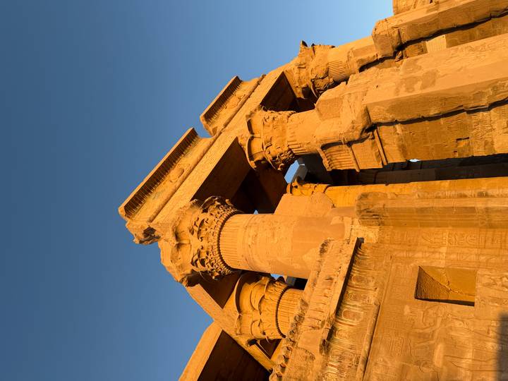 Golden light illuminates the sandstone columns and hieroglyphs of Kom Ombo Temple against a clear blue sky.