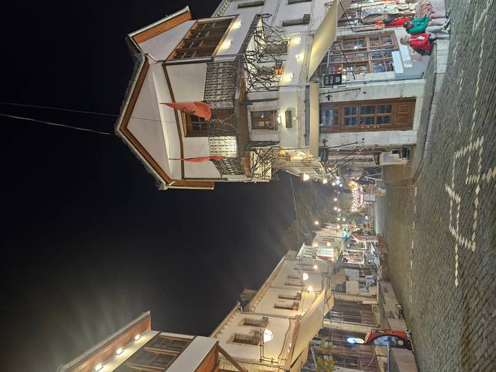 Night view of cobbled street in Gjirokastra old town lined with historic houses and Albanian flags.