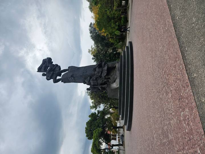 Large dark monument commemorating 1920 independence stands in open plaza under dramatic sky.