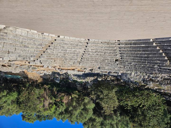 Stone amphitheatre seating curves around forested hillside in archaeological site of Butrint.