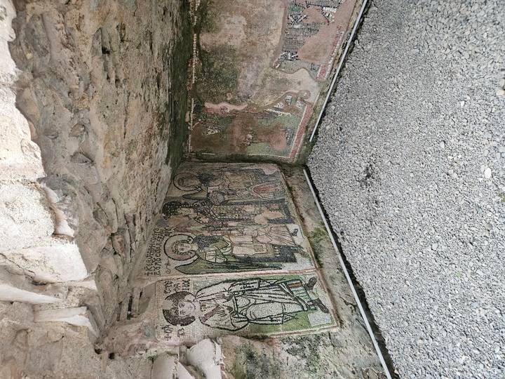 Colorful floor mosaics depicting saints and animals preserved in a sheltered archaeological niche.