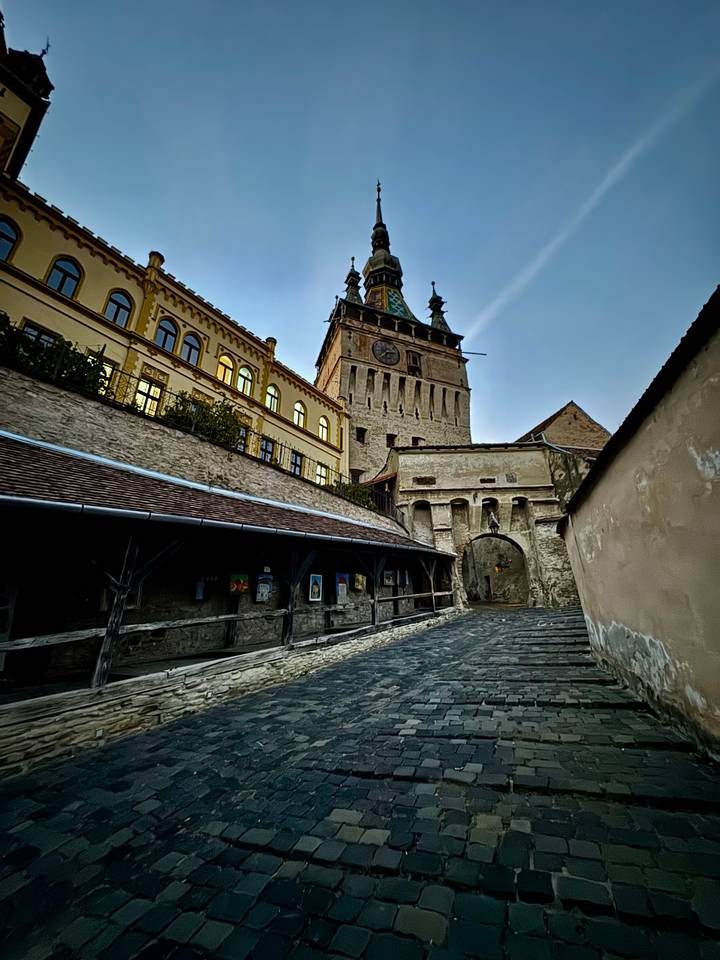 Tilted view of Sighisoara Clock Tower and medieval gate along empty stone street.