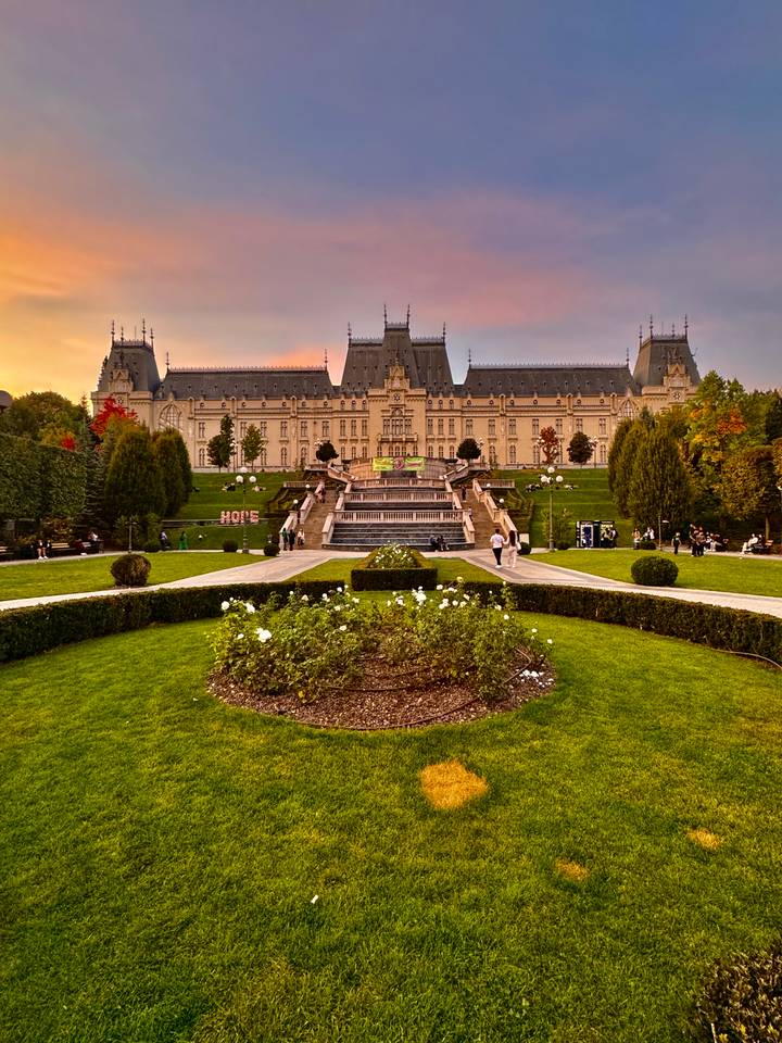 Palace of Culture in Iași at sunset with manicured gardens and visitors strolling.