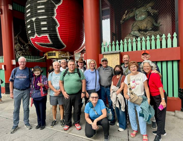 Tour group smiling beneath the giant red lantern of Kaminarimon gate at Senso-ji Temple.