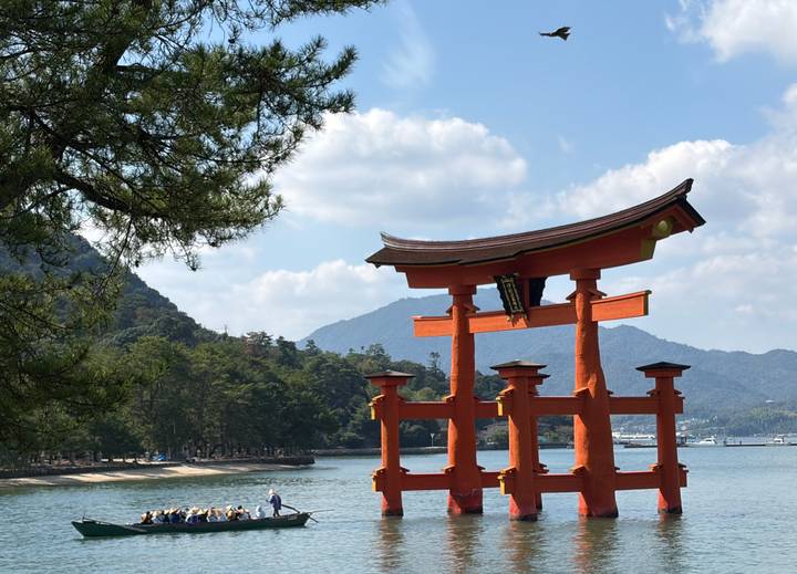 Iconic orange torii gate of Itsukushima Shrine standing in the bay with mountains behind.